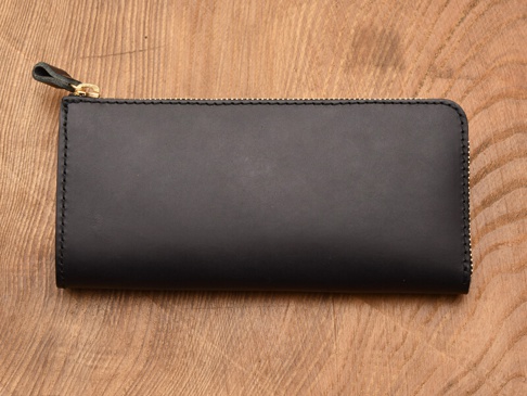 職人手作皮革Organ雙拉鍊L型長夾，黑色牛皮材質，L型開口設計，配有金色拉鍊及同色系皮革拉頭，置於木紋背景上。