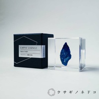 一個透明立方體內嵌著一顆深藍色、帶有金色斑點的青金石礦石，旁邊是一個深藍色的盒子，盒蓋上印有「LAPIS LAZULI」及日文「ラピスラズリ | 深淵な知性」。