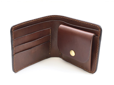 職人手作的經典棕色皮革雙折短夾，打開後呈現多個卡片夾層及一個附有金色按鈕的掀蓋式零錢袋。