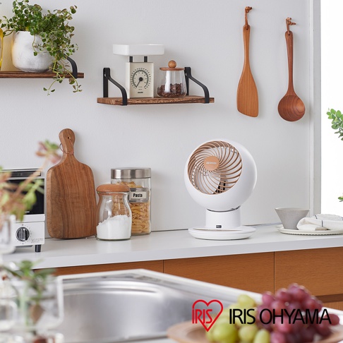 白色的圓形機身，搭配木紋色扇葉的空氣循環扇，擺放在廚房檯面上，旁邊有木質砧板、玻璃罐裝調味料和義大利麵。