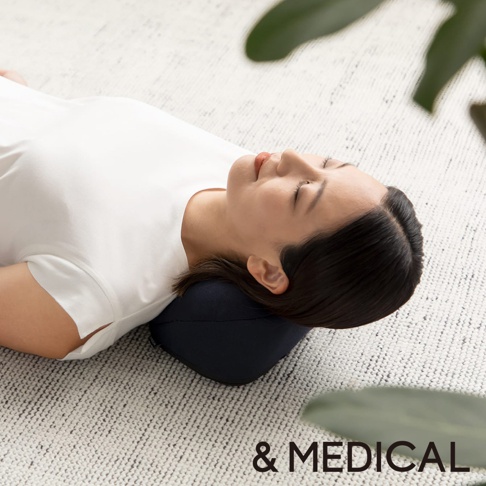 深藍色肩頸按摩紓壓枕，材質為柔軟織物，設計符合人體工學，能支撐頭部與頸部。一名女性仰躺，頭部枕於枕上，閉眼休息。