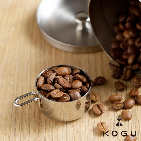 日製18-8不鏽鋼儲豆罐，附有10克量匙，罐身為銀色不鏽鋼材質，盛裝著淺棕色的咖啡豆。