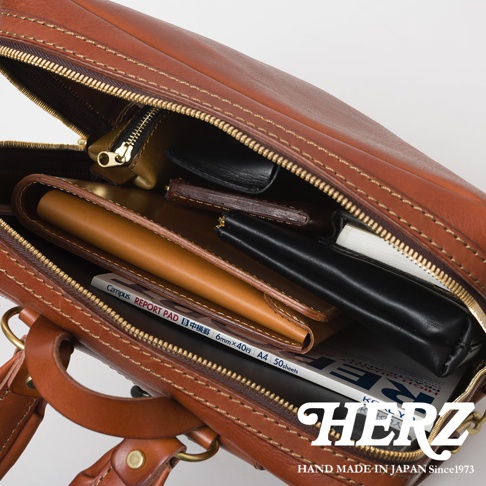 職人手作皮革軟皮商務後背包，展示內部收納，可見棕色皮革、筆記本、錢包及小物，搭配金色拉鍊。