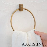 輕奢黃銅圓形毛巾環，固定在白色紋理牆面上，環體呈現金屬光澤，下方掛著一條蓬鬆的白色毛巾，一隻手正將毛巾掛上。