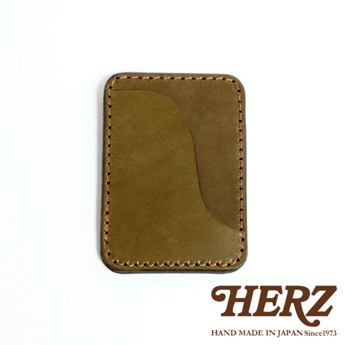 HERZ 品牌字樣，下方為 HAND MADE IN JAPAN Since1973。 產品為一個橄欖綠色皮革名片夾，以手工車縫線邊緣，並有兩個不同顏色的皮革層疊設計。