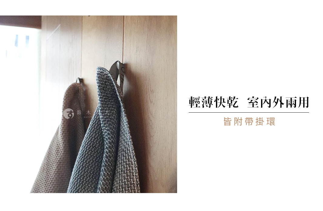 兩條紋理浴巾掛在木牆上的掛鉤上，其中一條浴巾上有「SUZUKI」的日文標誌，右側有「輕薄快乾 室內外雨用 皆附帶掛環」的文字說明