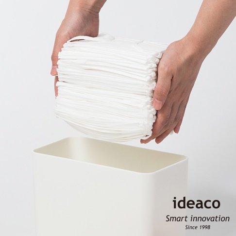 雙手正將一疊白色口罩放入白色長方形抽取盒中。