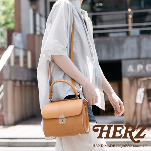 職人手作皮革復古杜勒斯手提包，採用天然棕色皮革製成，配有圓形提把、可調節斜背帶及金色鎖扣，包身線條俐落，復古風格明顯。