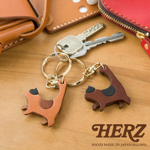 職人手作皮革貓咪造型鑰匙圈，共兩款顏色：淺棕色與深棕色。每個鑰匙圈皆為皮革製成，造型為簡約的貓咪，搭配金屬鑰匙圈及掛鉤。