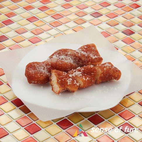 盤子上有三塊裹著糖的油炸麻花點心，背景是多彩的菱形馬賽克圖案。