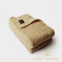 兩條淺黃色純棉長毛巾疊放，其中一條毛巾上可見深棕色品牌標籤。