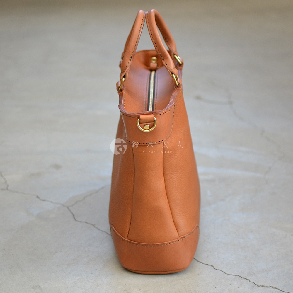 職人手作皮革Organ兩用商務托特包，採用溫暖的棕褐色皮革，雙提把設計，側邊有可拆卸的D型金屬環，搭配金色拉鍊，整體呈現簡約大方的風格。