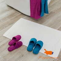 浴室地板上擺放著一塊白色毛巾，旁邊有兩雙竹棉混紡室內拖鞋，一雙為紫色，另一雙為藍綠色。浴缸旁掛著兩條毛巾，一條為紫色，另一條為藍綠色。