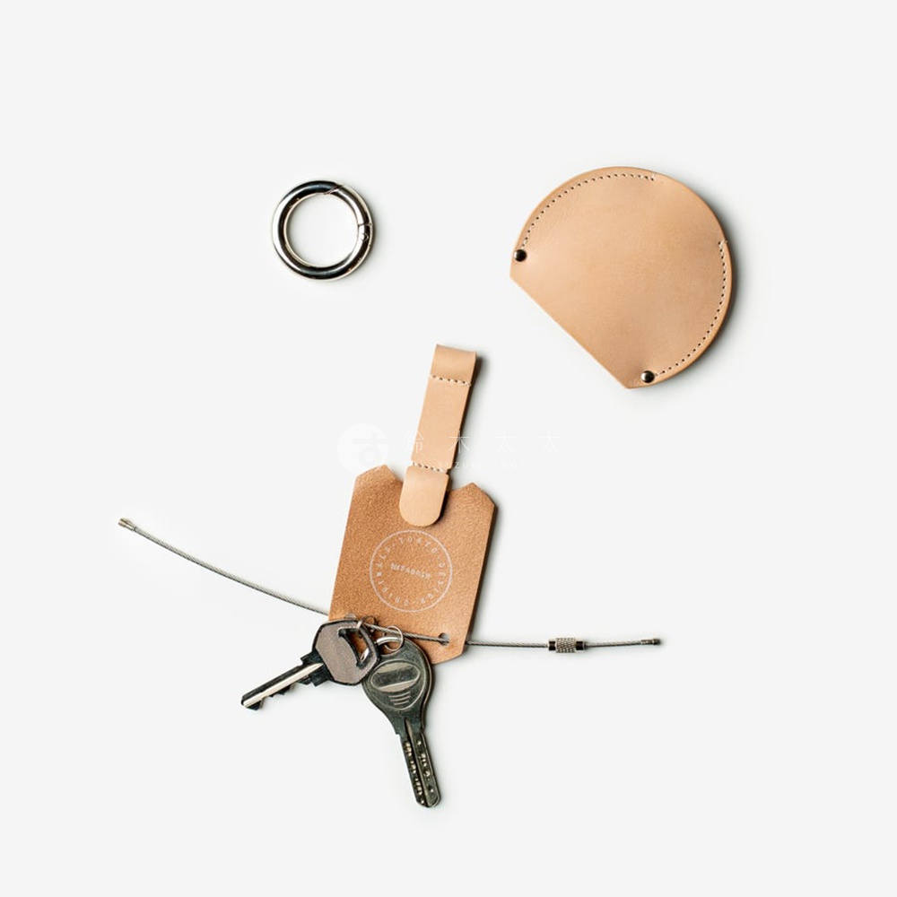 皮革圓形鑰匙收納圈，附掛著兩個鑰匙和一個吊牌，旁邊還有一個圓形金屬環。