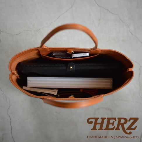 職人手作皮革Organ肩背托特包，內部空間展示，可放入手機、皮夾、筆記本和文件夾，包包為棕褐色皮革材質，提把設計。HERZ HAND MADE IN JAPAN Since1973。