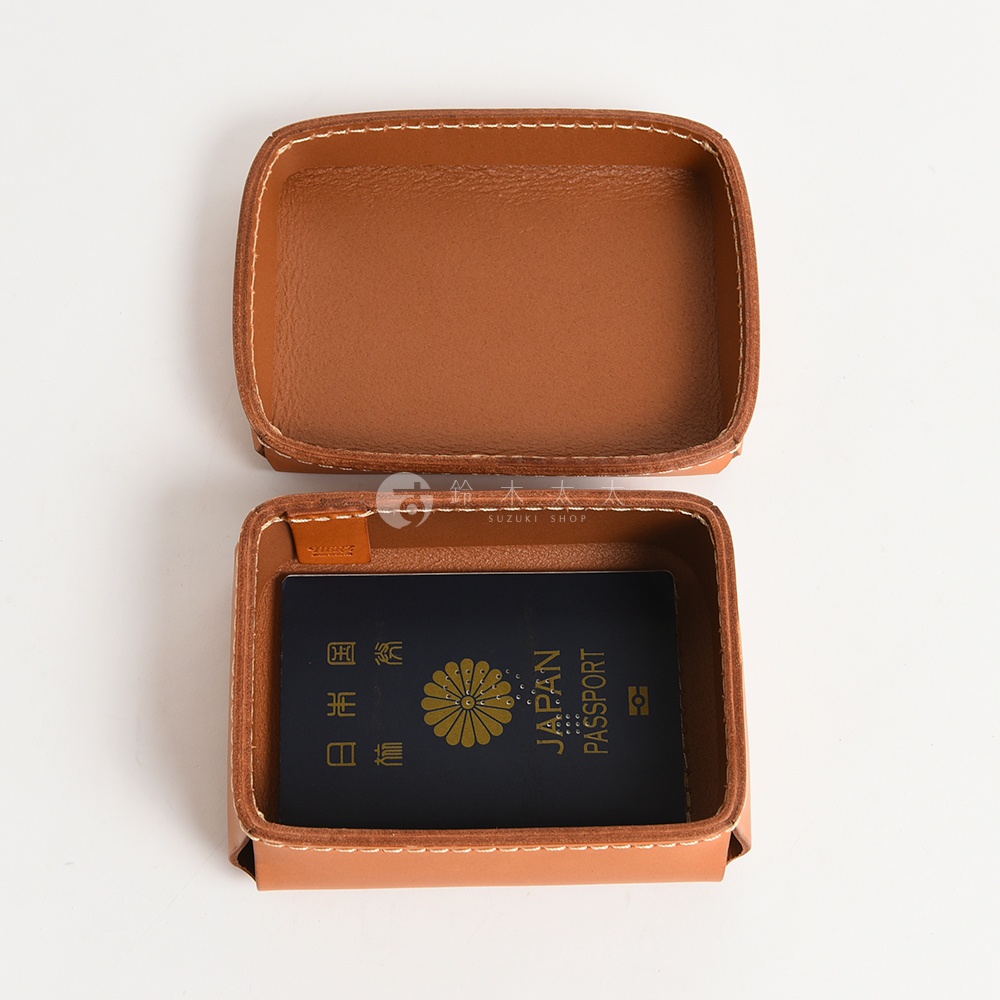 職人手作皮革小物收納盒 KZ-5 S，採用 tan 色皮革製成，縫線整齊。盒內放置一本深藍色護照，護照上有金色菊花圖案及「JAPAN PASSPORT」字樣。