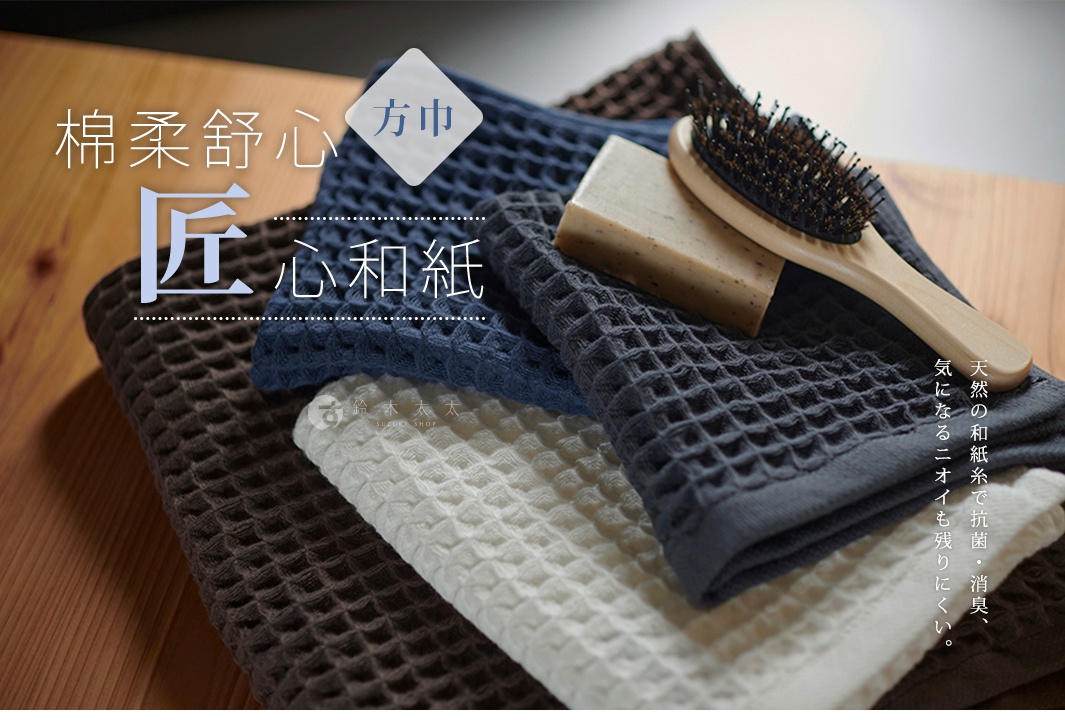 多條和紙紋理方巾疊放，中間有肥皂和木柄毛刷，背景為木紋。