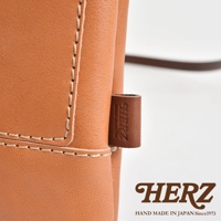 咖啡色皮革直式隨身單肩包，車縫線清晰，帶有品牌皮革小標籤，簡約實用。