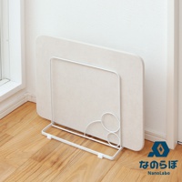 雙面珪藻土瞬間吸水地墊，米白色，厚實，圓角設計，立於白色金屬支架上，置於木質地板與白色牆壁的角落。