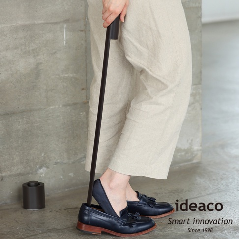 ideaco Smart innovation Since 1998，一位女士穿著米白色長褲和黑色樂福鞋，正使用長柄鞋拔穿鞋。