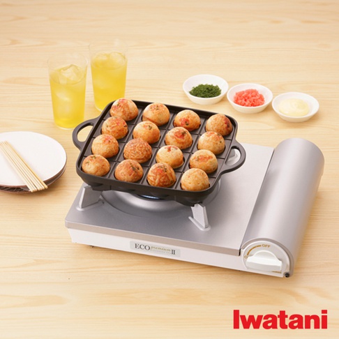 節能高效瓦斯爐Eco Premium II CB-EPR-2，銀白色機身搭配黑色烤盤，烤盤上擺滿了十八顆金黃色、圓滾滾的章魚燒，右側有三個白色小碟，分別裝有綠色蔥花、粉紅色薑末和白色醬料，背景是兩杯黃色飲料和兩個白色盤子，其中一個盤子上放著竹籤。