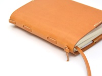 職人手作皮革附繩書套，採用天然棕褐色皮革，以手工縫線固定，側邊有皮革繩束，適合放入 S 尺寸筆記本。