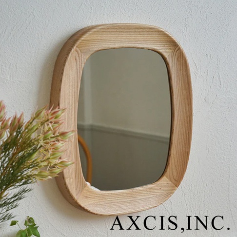 橢圓形鏡面，邊框由淺木色天然木材製成，表面有明顯的木紋。鏡子掛在有紋理的白色牆壁上，左側有一束粉綠色和粉紅色的裝飾植物。