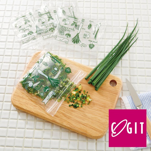 透明塑膠密封保鮮袋，印有綠色蔬菜圖案，內含切碎的蔥，另有一疊未開封的同款保鮮袋。右側擺放一束新鮮青蔥，旁邊是木質砧板和一把刀。