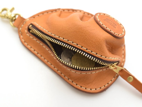 職人手作皮革餃子造型零錢包，採用天然棕色皮革製成，帶有黃銅色拉鍊和鑰匙圈。包包縫線清晰，餃子造型飽滿，內部可見部分硬幣。