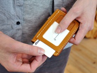 雙手操作的棕色皮革三面雙折票券收納夾，內有透明卡槽，可見卡片標誌「HERZ」和「Craftsmanship」。