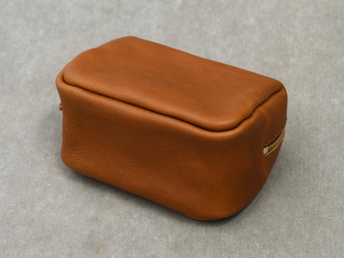一個棕褐色的皮革拉鍊收納包，造型簡潔，材質柔軟，呈現出職人手作質感。