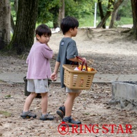 一個男孩提著一個棕色塑膠籃子，裡面裝有零食，籃子旁邊站著另一個男孩，兩人走在戶外。