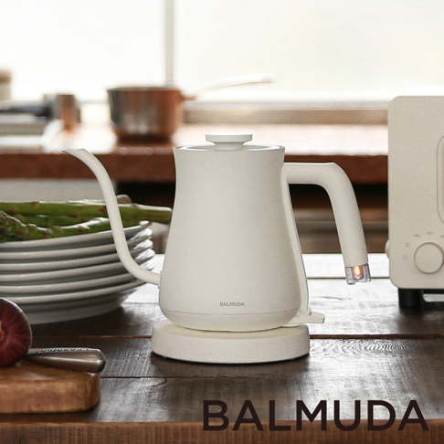 白色 BALMUDA 絕美手沖壺，設有細長壺嘴和弧形提把，放置於圓形白色底座上，壺身印有 BALMUDA 標誌。