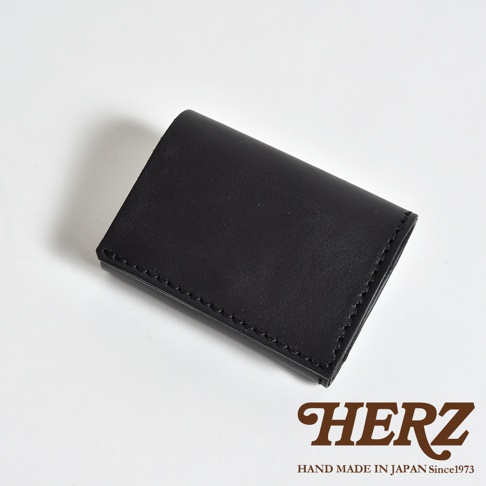 日本職人品牌 HERZ 手作黑色皮革三折式短夾，採用柔軟牛皮製作，設計簡潔俐落，體積輕巧適中，下方標註品牌名稱與日本手工製造資訊。