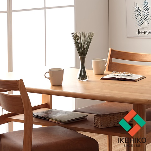 木質餐桌上擺放著一個玻璃花瓶，瓶內插著細長的綠色藺草。旁邊有兩個米白色馬克杯，以及一本打開的書和一副眼鏡。桌子下方可見木質餐椅的座位，椅面為棕色皮革。