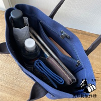 藍色帆布水桶托特包，內有摺疊傘、水瓶、筆記本、錢包和卡夾，包內有拉鍊內袋和掛扣。