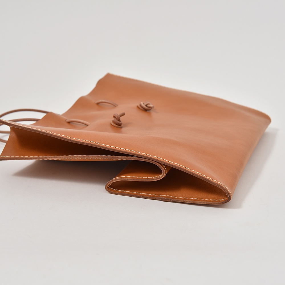 一個焦糖色皮革製成的提袋，以白色縫線裝飾，袋口處有兩個皮革繩結。