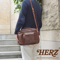 職人手作的深棕色皮革多功能收納單肩包，配有頂部提把、可拆卸肩帶，正面有三個拉鍊口袋和一個附加的開放式口袋，包身線條簡潔，皮革質感良好。