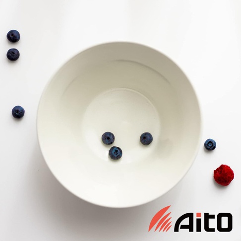 一個簡約的白色陶瓷深碗，碗內有四顆藍莓，碗外左側有三顆藍莓，右側有一顆覆盆子。