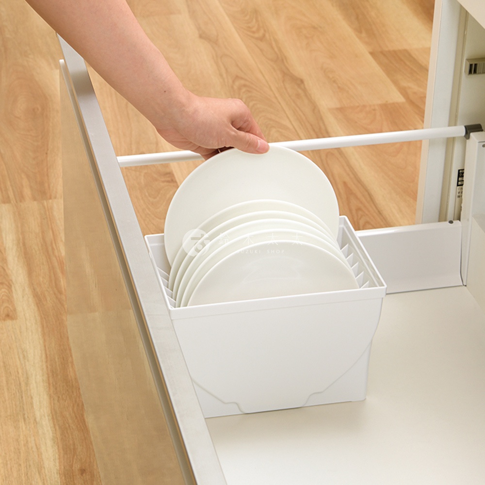 一只手正在將一疊白色盤子放入一個白色的抽屜式餐盤收納架中。