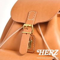 職人手作皮革經典後背包，以天然皮革製成，呈現溫潤的棕褐色澤，搭配復古黃銅色金屬扣環及縫線細節。