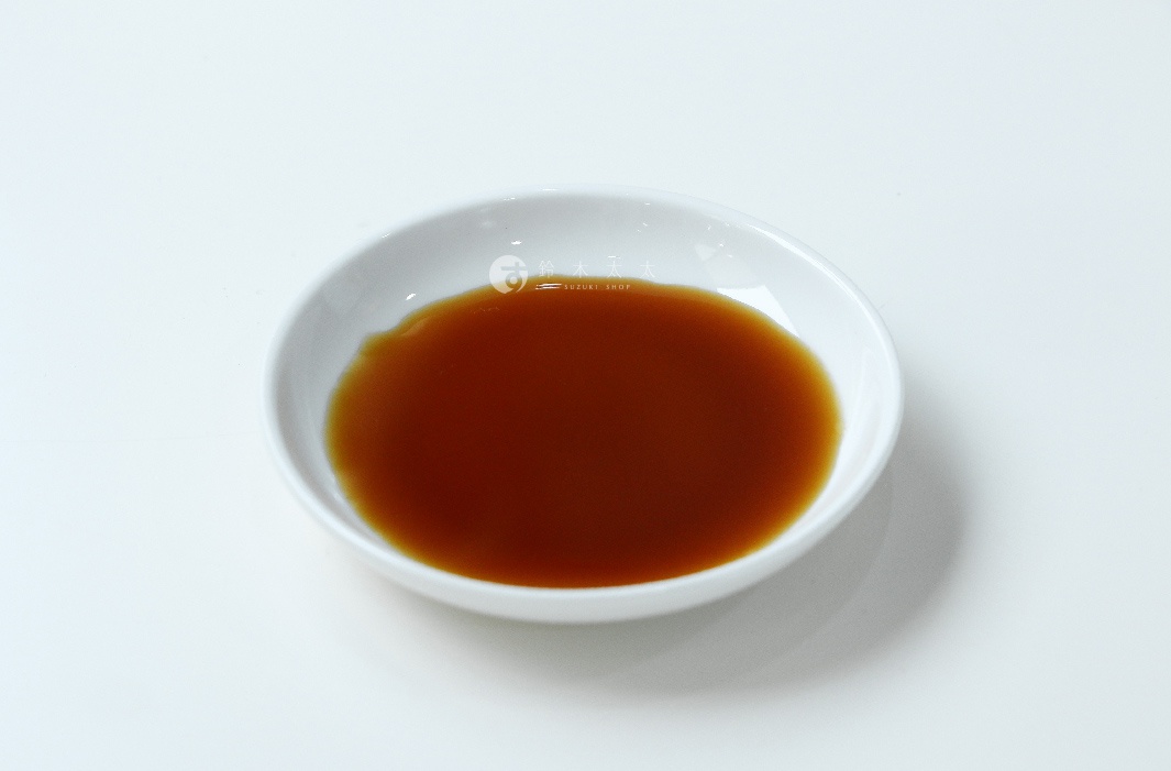 一個白色小碗中盛有琥珀色的液體，可能為森文柑橘醋調味料，碗邊緣有少許飛濺痕跡，背景為純白色。