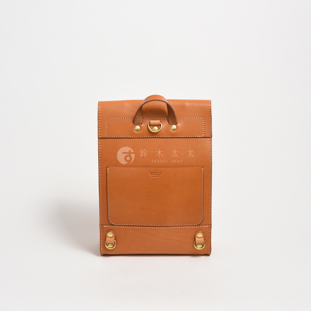 職人手作皮革紙袋風後背包，採用棕色皮革製成，設有頂部提把、前置口袋及金屬扣環，整體風格簡約。