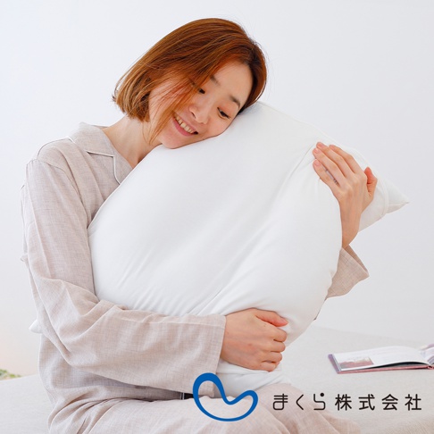 一名女性穿著淺棕色睡衣，懷抱著一個純白色的枕頭，枕頭表面光滑，材質疑似為親膚棉質。