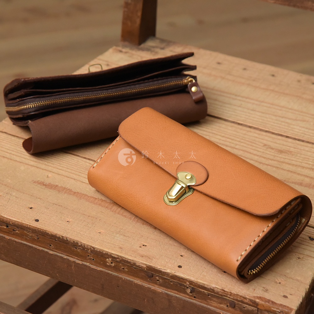 職人手作的淺棕色皮革長夾，採用手風琴式多卡層設計，配有金屬鎖扣和拉鍊，另一深棕色皮革長夾置於後方。