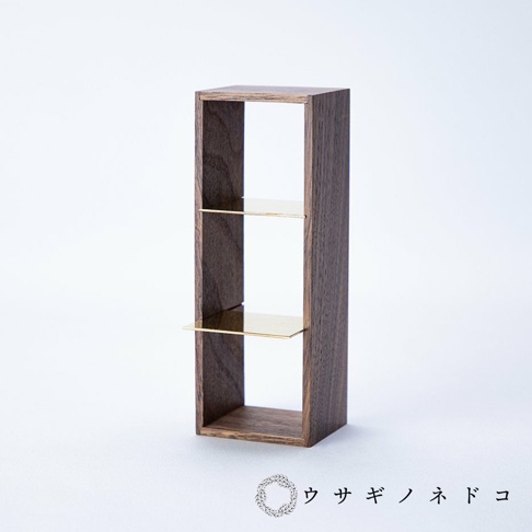 深色木質立方體結構，內有兩層金色層板，呈垂直三層收納設計。