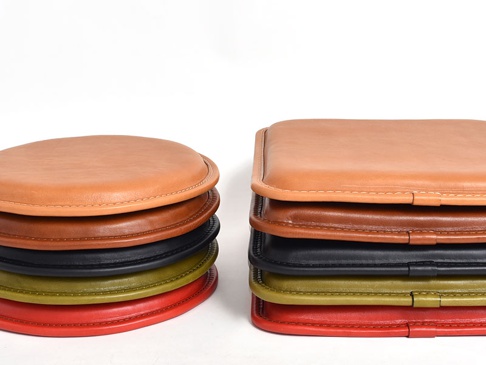 職人手作皮革方形坐墊，展示多種顏色堆疊，包括淺棕色、深棕色、黑色、橄欖綠及紅色。坐墊表面光滑，邊緣有細緻車縫線，材質為皮革。