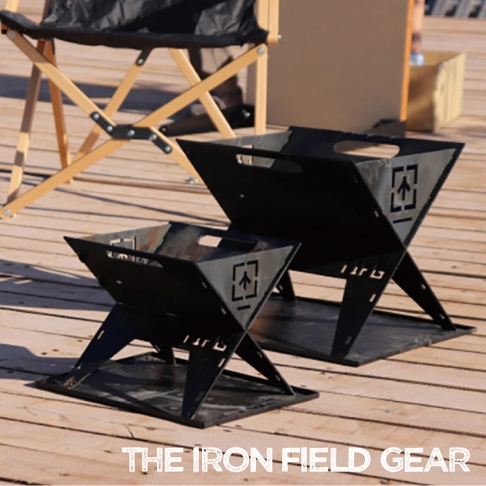 TAKI BEITA焚火台爐架套裝 S，黑色金屬材質，呈四方錐形，兩側有提把，正面有箭頭標誌切割。一組兩個，大小不同，放置於木製地板上，背景有露營椅。