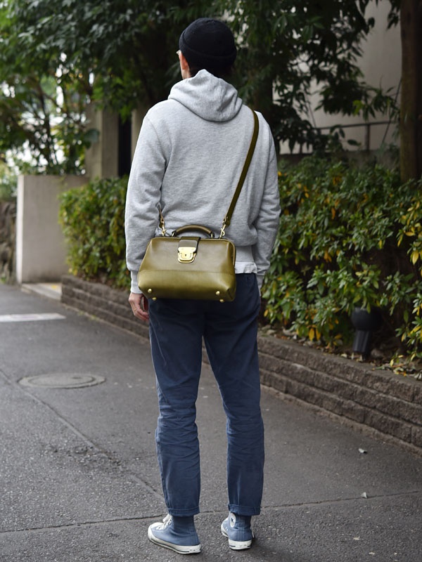 橄欖綠皮革迷你口金包，帶有金色鎖扣和可拆卸肩帶，由男性斜挎於身。