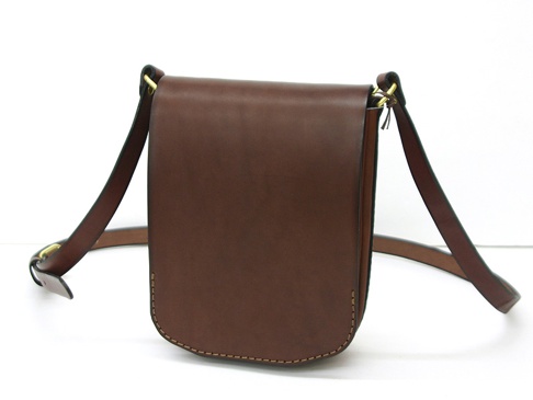 職人手作皮革翻蓋直式單肩包，採用深棕色光滑皮革製成，配有可調節的深棕色皮革肩帶和金色金屬釦環，整體設計簡約，邊緣有縫線裝飾。